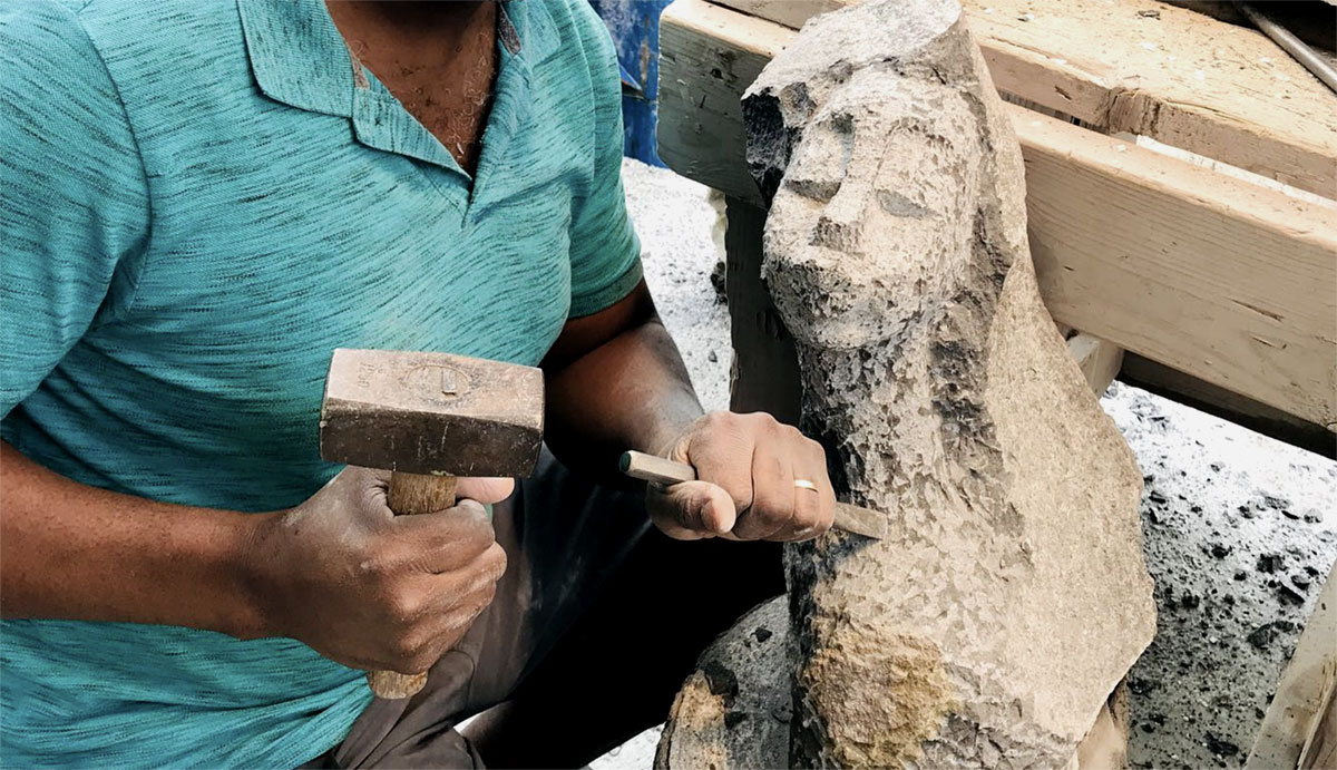 Sculptor carving a block of stone surrounded by stone dust